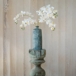 Decorative vase with white flowers on a wooden pedestal against a striped wall.