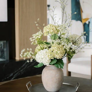 Decorative flower arrangement in a textured vase on a table with a blurred indoor background