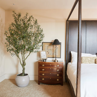 Luxurious interior with CG Hunter Artificial Olive Tree 8.5' in Artisan Mediterranean Pot, placed beside a wooden nightstand in a stylish bedroom setting.