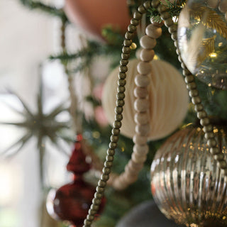 Close-up of the 4" Mercury Ribbed Glass Antique Gold Ornament by CG Hunter, highlighting its delicate craftsmanship and opulent finish, complemented by natural wooden beads and chic holiday decor.