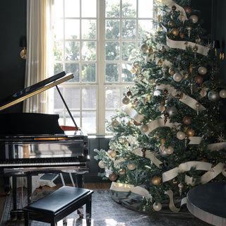 Elegant holiday decor scene featuring a sophisticated Christmas tree adorned with neutral palette glass finial ornaments by CG Hunter, complemented by a grand piano.
