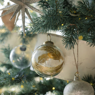 An elegant close-up of the 3" Artisan Glass Gold Etched Leaf Ornament by CG Hunter hanging on a Christmas tree, featuring luxurious gold etchings that enhance its festive appeal.