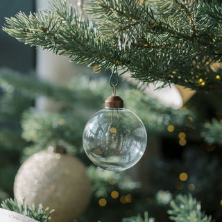 A stunning clear glass ornament hanging from a Christmas tree, surrounded by twinkling lights and warm textures, featuring CG Hunter's 2.25" Clear Glass Ornament, perfect for adding a luxurious touch to holiday celebrations.