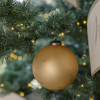 Close-up of a stunning matte antique gold glass ornament hanging among twinkling lights on a holiday tree, showcasing the opulence of CG Hunter's 4" Matte Antique Gold Glass Ornament collection.