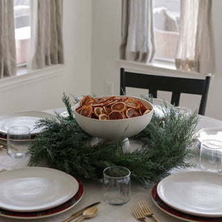 Chic dining table centerpiece featuring a 30-inch Faux Evergreen Cedar Wreath by CG Hunter, beautifully paired with dried orange slices for a luxurious touch.