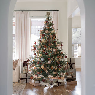 Gorgeous holiday setup featuring a 5" Mercury Marble Glass Ornament by CG Hunter on a lavishly decorated Christmas tree, surrounded by seasonal gifts.