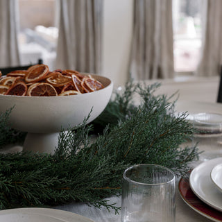 Beautiful dining table centerpiece with 30" Faux Evergreen Cedar Wreath by CG Hunter, complemented by dried oranges and sophisticated tableware.