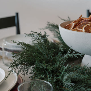 Close-up of a dining setting showcasing the 30" Faux Evergreen Cedar Wreath by CG Hunter, adorned with dried oranges, exuding luxury and elegance.