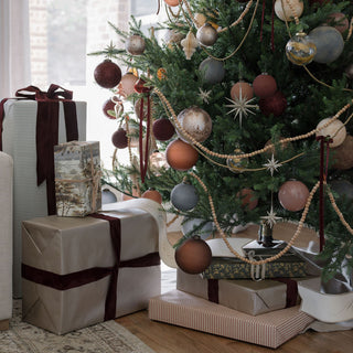 Delicate display of the 5" Frosted Cinnamon Glass Ornament by CG Hunter, complemented by elegantly wrapped gifts under a meticulously decorated Christmas tree.
