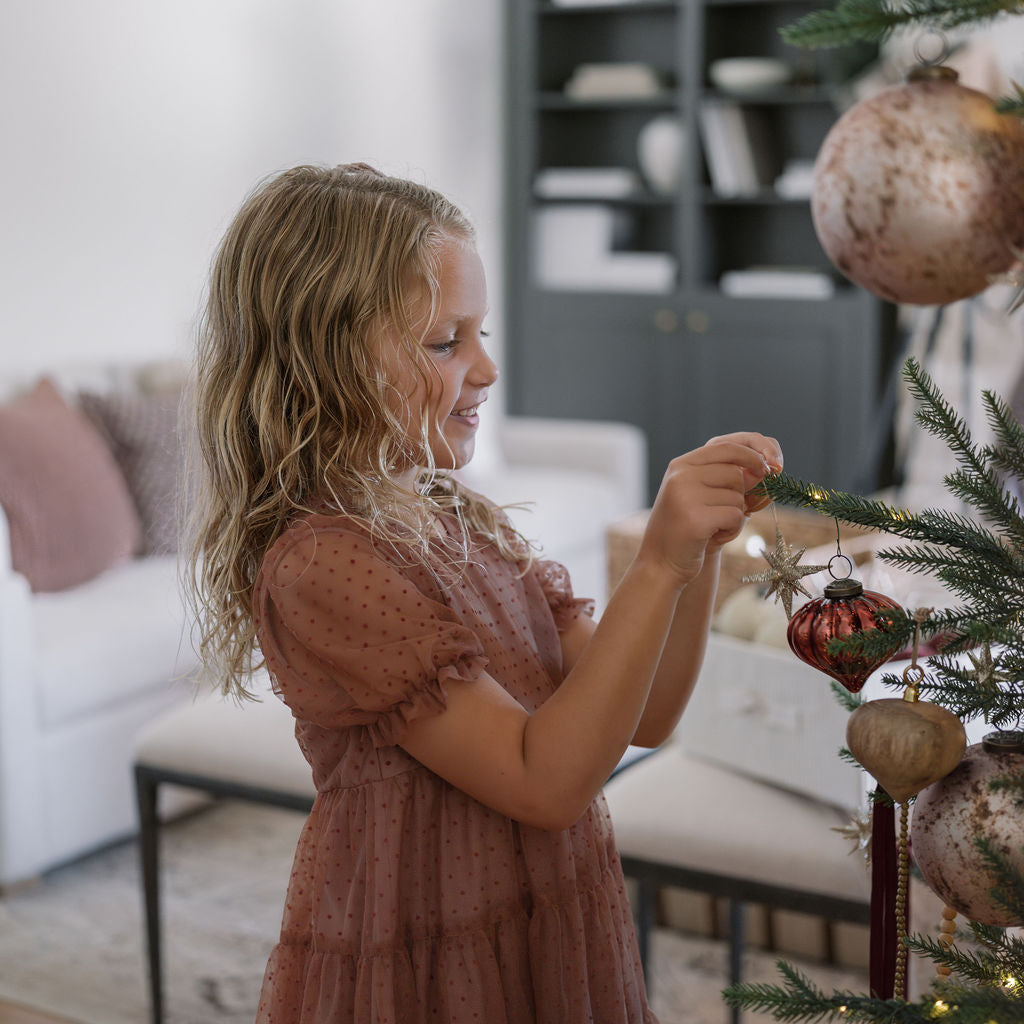 Young girl in awe of the beauty of the timeless collection tree placing ornament on tree