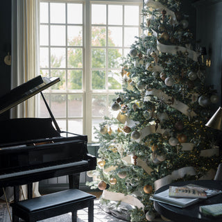 A beautifully decorated Christmas tree in a sophisticated interior, adorned with luxurious ornaments and ribbons, creating a festive ambiance inspired by CG Hunter's 4" Matte Antique Gold Glass Ornament.