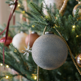 Elegant 4" Textured Slate Blue Glass Ornament by CG Hunter, hanging amidst a festive Christmas tree, radiating sophistication and charm for the holiday season.