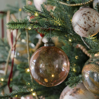 Beautifully handcrafted 5" Mercury Marble Glass Ornament by CG Hunter, reflecting soft light as it hangs amongst other luxurious holiday decorations on a Christmas tree.