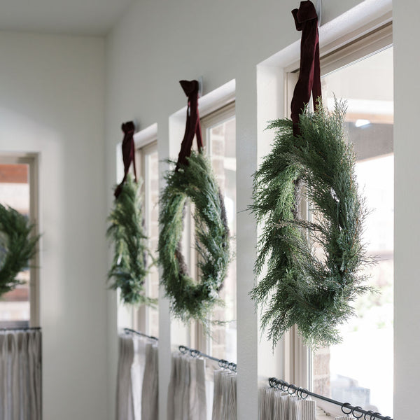 Angle of 30" Lifelike Cedar Wreath on window hanging with wide velvet ribbon