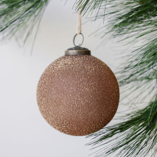 Luxurious 4" Textured Cinnamon Glass Ornament by CG Hunter, featuring a sparkling, handcrafted design, elegantly hanging amidst green pine branches.