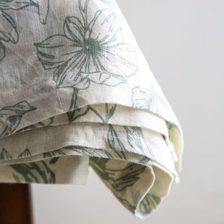 Close-up of the luxurious CG Hunter Grey and Green Lilies Linen Tablecloth showcasing intricate lily patterns, embodying refined elegance for any dining occasion.