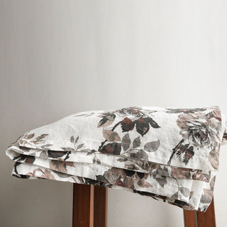 Refined look at the CG Hunter Handcrafted Linen Eggplant and Grey Roses Tablecloth resting on a wooden surface, showcasing its artistic gray rose motifs and premium linen texture.