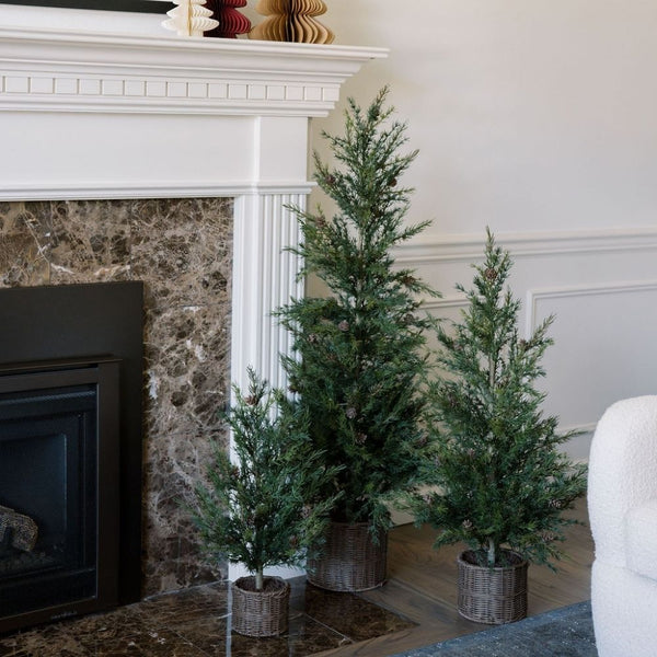 Group of three CG Hunter 2' Pine Trees arranged stylishly near a sophisticated fireplace, enhancing the festive atmosphere with their natural beauty and charming rustic base.