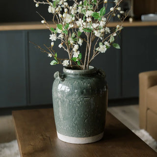 Green textured vase with white flowers on a wooden table in a room setting