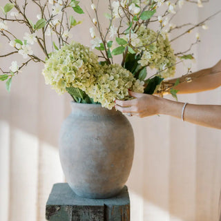 Person arranging flowers in a textured vase against a neutral background
