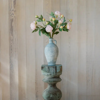 Vintage-style vase with flowers on a wooden pedestal against a wooden wall.