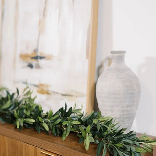 Decorative greenery on a wooden surface with a white vase in the background