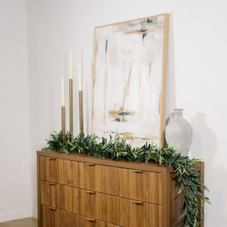 Wooden dresser with greenery and candles against a white wall