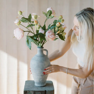 Woman holding a vase with pink flowers against a neutral background