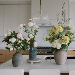 Two flower arrangements in vases on a kitchen counter with a modern kitchen background.