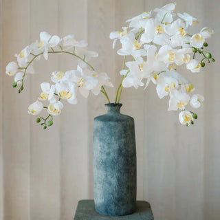 White flowers in a textured blue vase against a neutral background