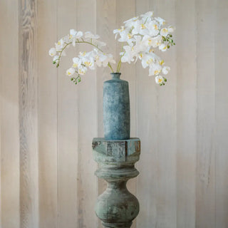 Decorative vase with white flowers against a wooden paneled wall