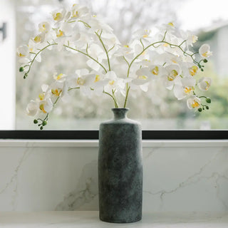 White flowers in a gray marble vase on a marble surface with a blurred window background