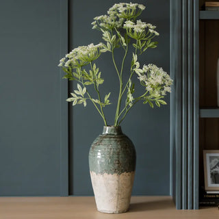 Decorative vase with green and white flowers against a dark wall.