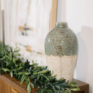 Decorative vase with green and beige gradient on a wooden surface with greenery