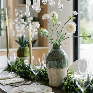 Decorative table setting with a vase of white flowers and greenery.