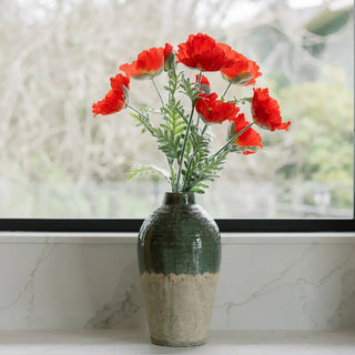 Green vase with red flowers on a marble surface with a blurred natural background
