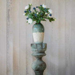 Decorative vase with flowers on a wooden pedestal against a wooden panel background
