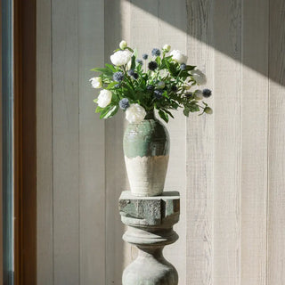 Decorative vase with flowers on a pedestal against a wooden wall.