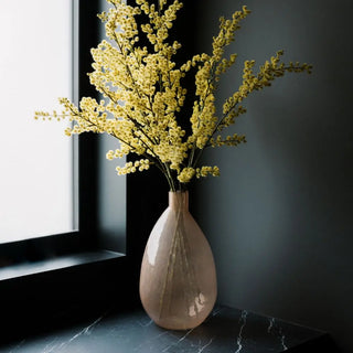 Beige vase with yellow flowers on a dark surface near a window