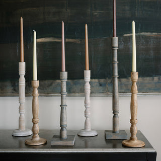 Charming collection of tapered candle holders crafted from white mango wood by CG Hunter, featuring a mix of natural finishes, elegantly set against a contemporary art backdrop for a refined aesthetic.