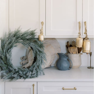 Beautifully styled 30" Flocked Cedar Wreath by CG Hunter, positioned on a kitchen counter with rustic decor, adding a chic and festive ambiance to home interiors.