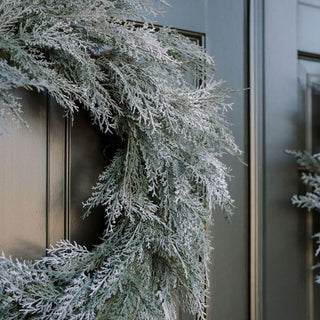 Elegant 30" Flocked Cedar Wreath by CG Hunter, adorned with frosty cedar branches, showcased on a dark front door, enhancing winter decor with a touch of luxury.