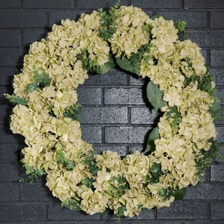 Floral wreath with light-colored flowers and green leaves on a brick wall background