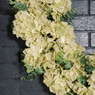 Close-up of a decorative wreath with light-colored flowers and green leaves against a dark background.