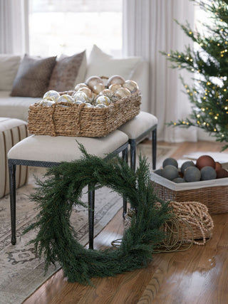 Refined living room setting with a 30-inch Faux Evergreen Cedar Wreath by CG Hunter, elegantly placed near decorative ornaments, creating a warm, inviting ambiance.