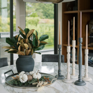 Stylish arrangement of tapered candle holders in white mango wood by CG Hunter on a marble table, surrounded by decorative elements, creating a sophisticated centerpiece for modern dining spaces.