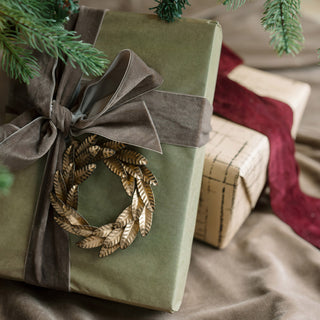 Elegant 5-inch iron wreath ornament in brass, beautifully attached to a gift wrapped in green paper. A luxurious decoration by CG Hunter, ideal for adding a sophisticated touch to holiday gifting.