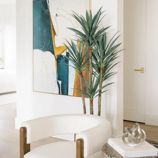 Modern interior with a plant, chair, and abstract painting on a white wall.