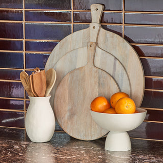 Elegant display of the Charlotte Round Wooden Serving Board Trio by CG Hunter, showcasing handcrafted wooden boards alongside a charming ceramic vase and fresh oranges, perfect for stylish entertaining.