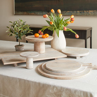 Charlotte Wood Serving Pedestal by CG Hunter, elegantly arranged on a dining table with vibrant flowers and fresh fruits, highlighting the artisanal charm of the collection.
